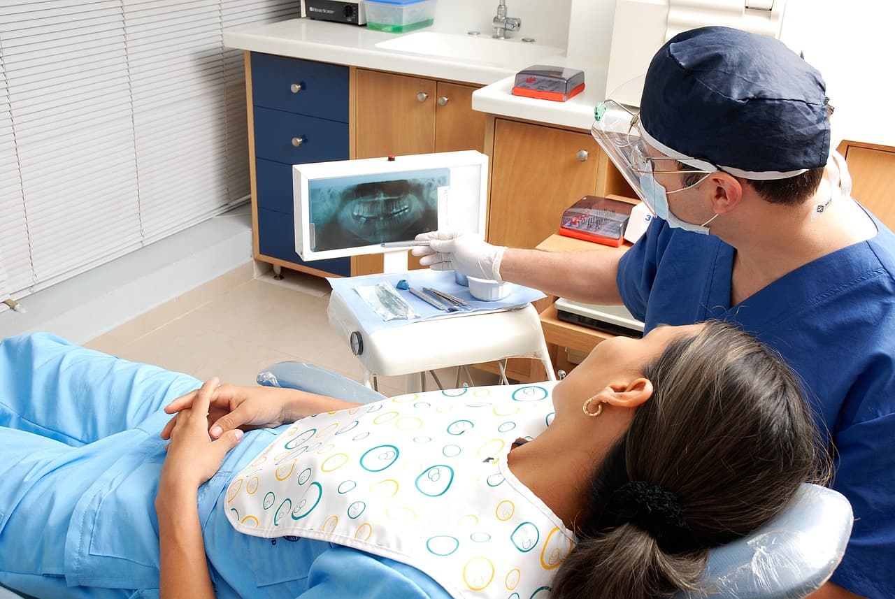 A patient in the chair while the dentist looks at her x-ray on screen