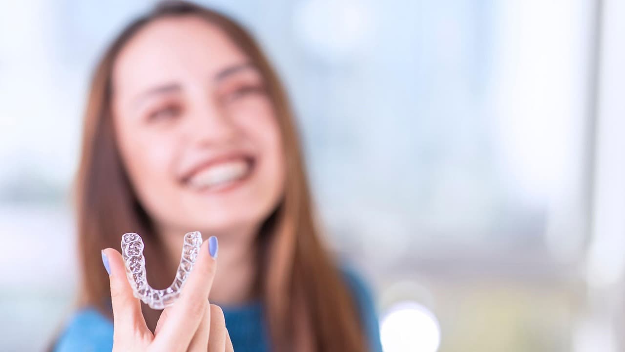 A smiling woman holding a clear aligner